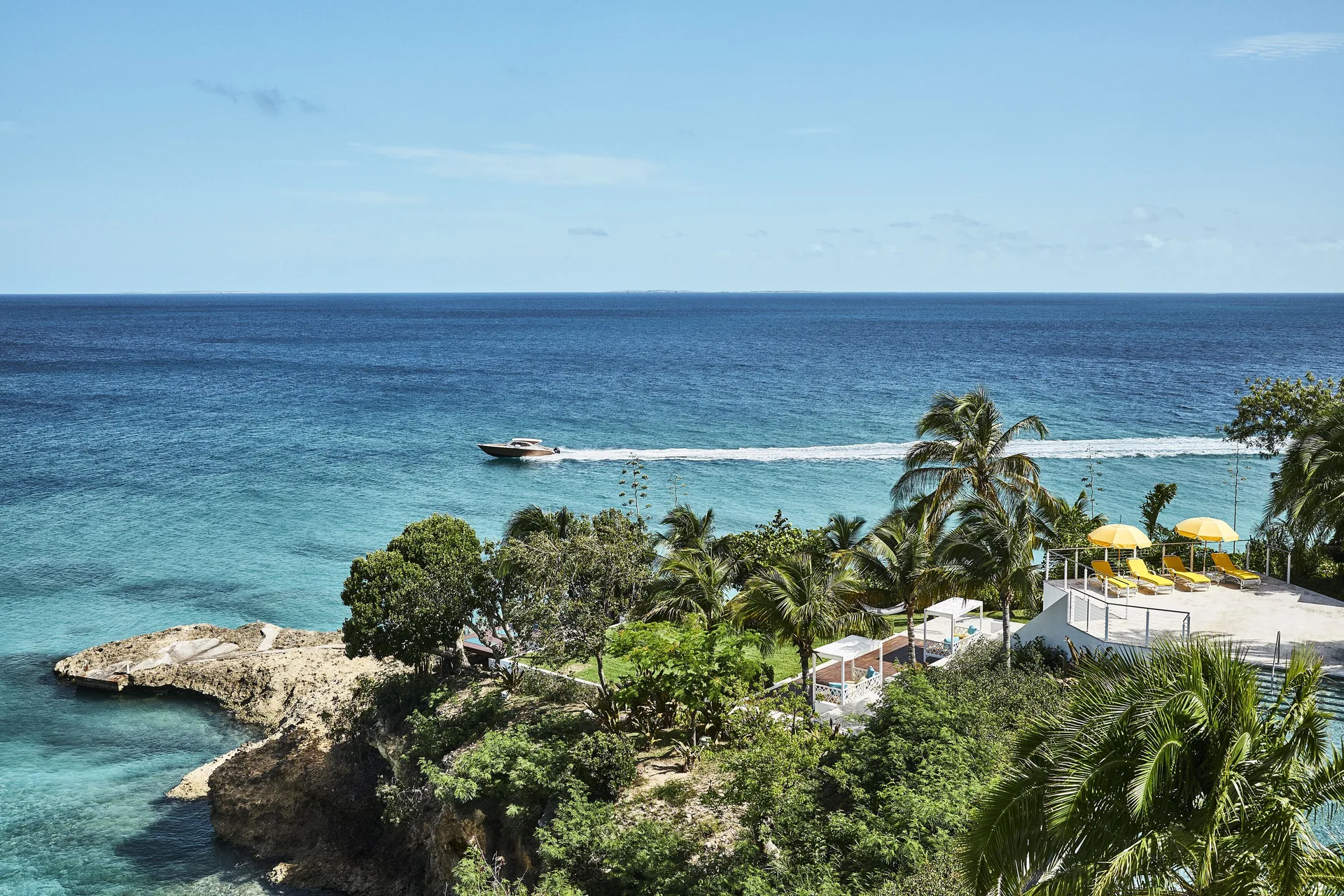 Clifftop palms, cabanas, yellow loungers, and a boat offshore at Malliouhana Resort Anguilla.