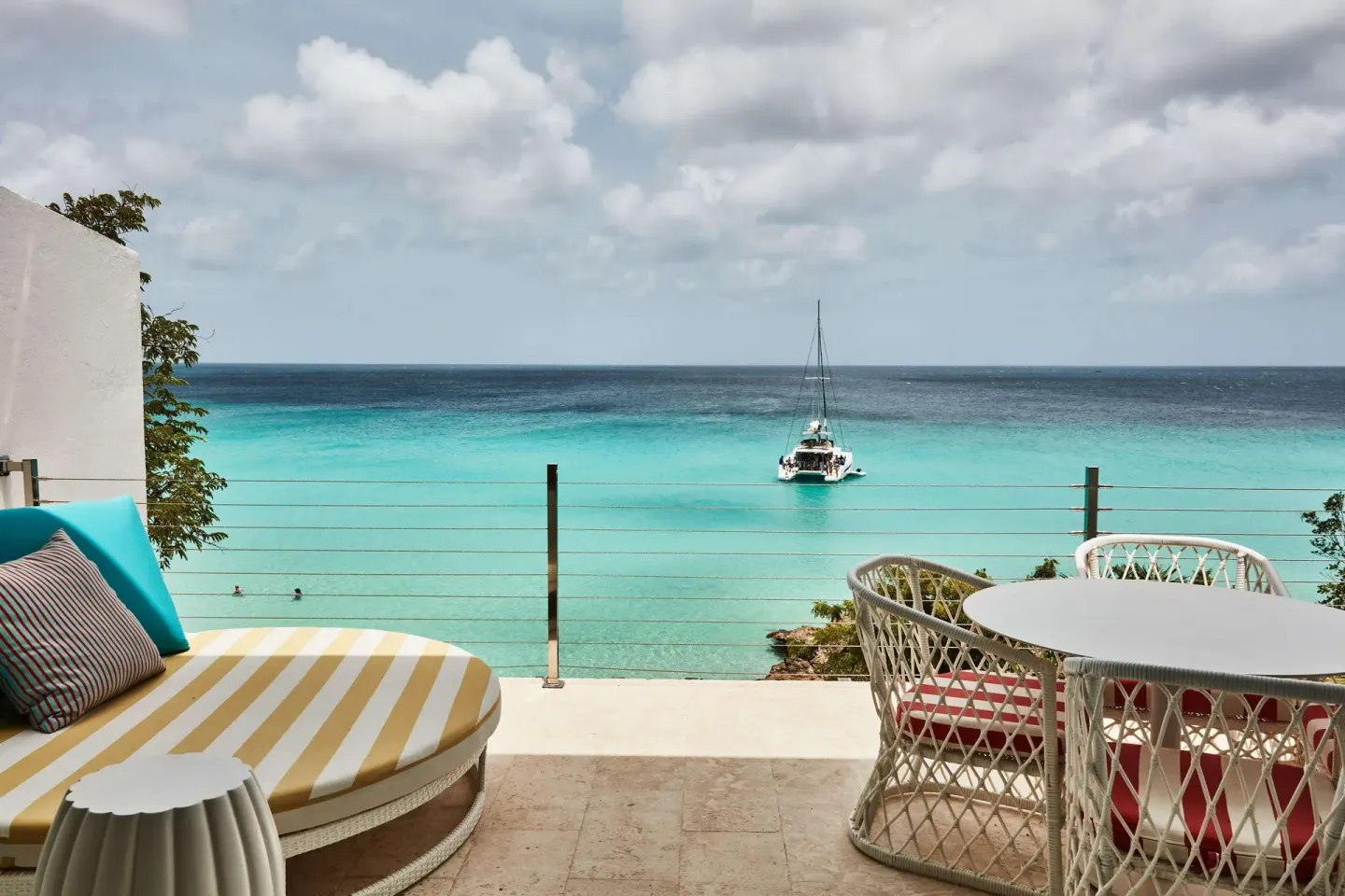 Oceanfront terrace with lounge seating and a sailboat at Malliouhana Resort Anguilla.