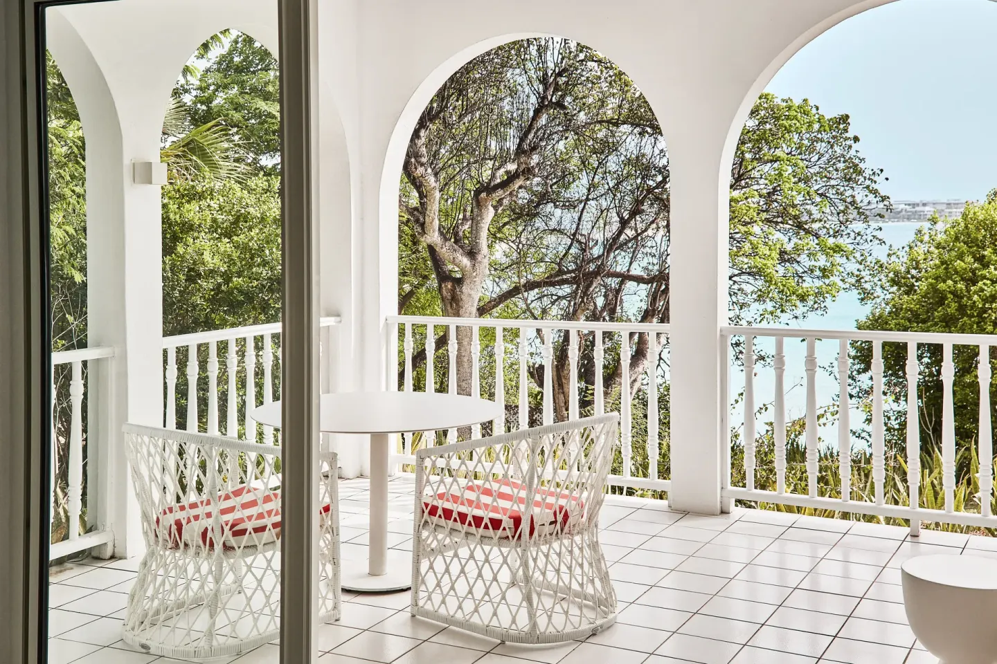 Garden View Deluxe balcony with chairs, arches, trees, and water glimpses at Malliouhana Resort Anguilla.