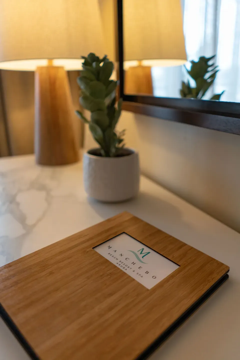 In-room guest directory with lamp, mirror and small plant at Manchebo Beach Resort and Spa.