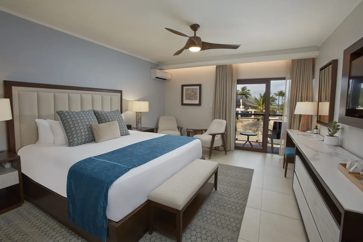 Guest room with a king bed, balcony doors and palm views at Manchebo Beach Resort and Spa.
