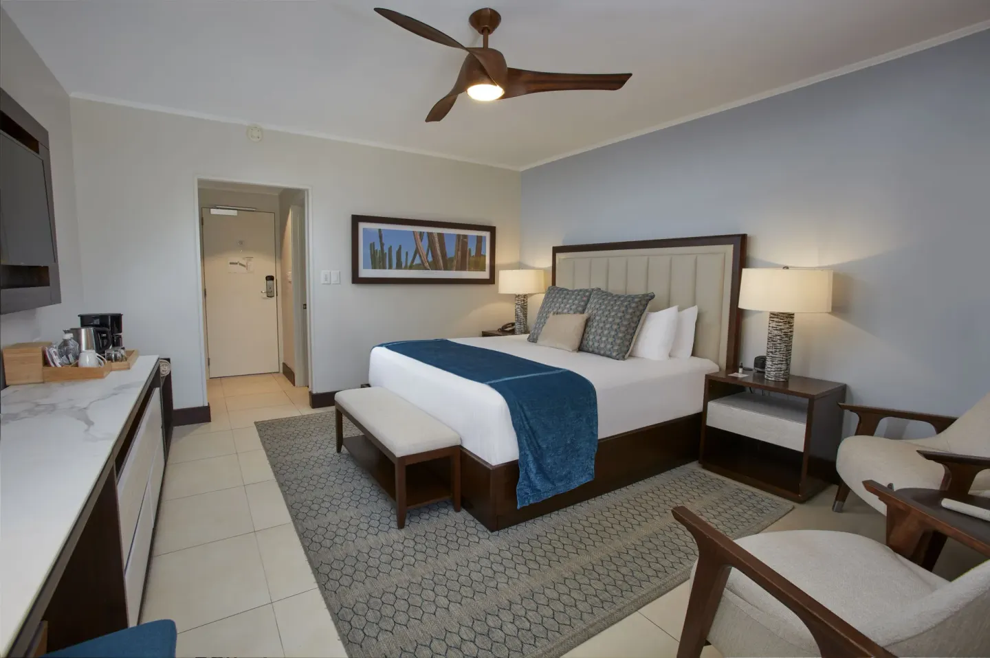 Guest room with a king bed, armchairs, desk counter and entry door at Manchebo Beach Resort and Spa.