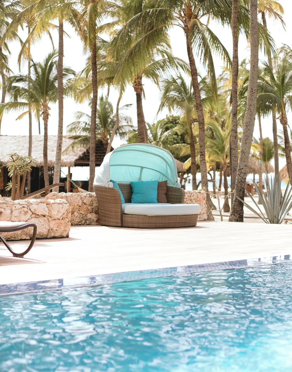 Poolside daybed with turquoise canopy among palms at Manchebo Beach Resort and Spa.