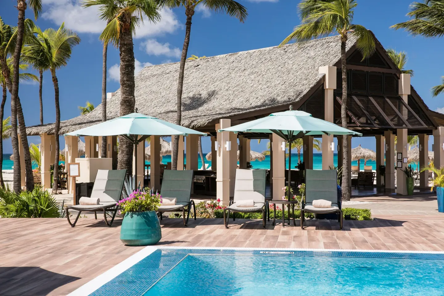 Poolside lounge chairs beside a thatched pavilion at Manchebo Beach Resort and Spa.