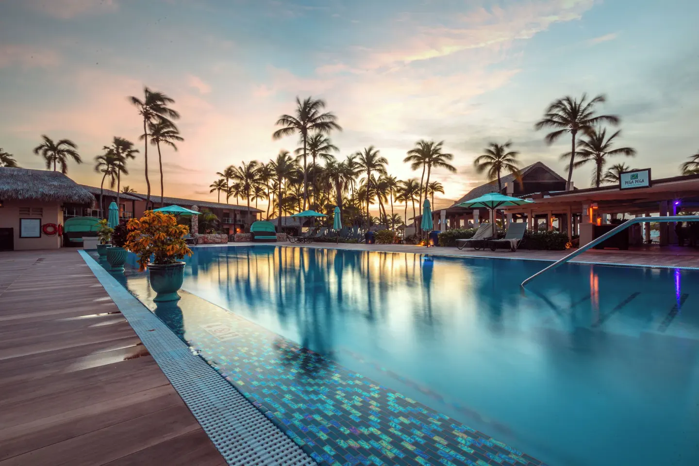 Sunset pool view with palms and Pega-Pega sign at Manchebo Beach Resort and Spa.