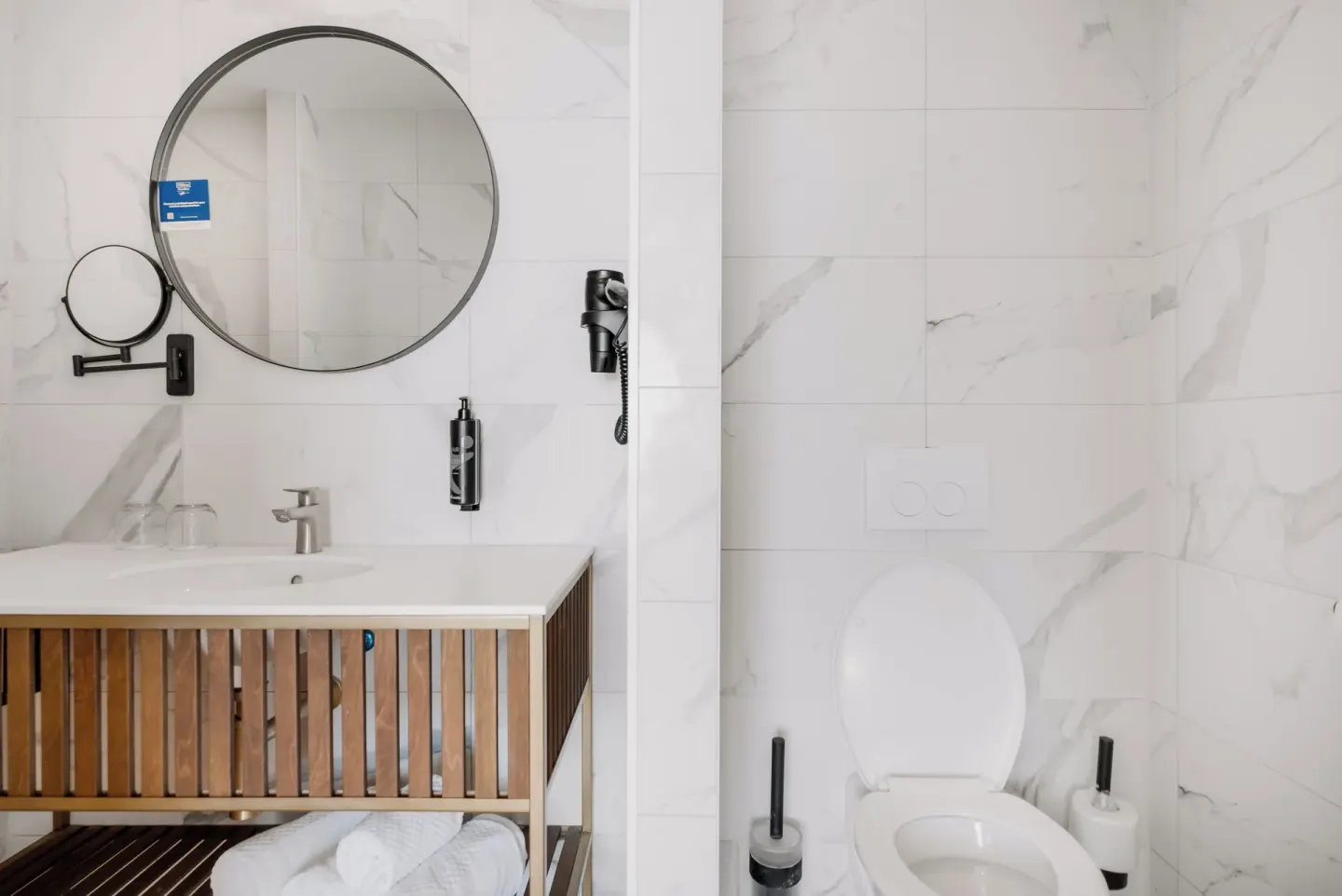 Bathroom vanity and toilet at Mangrove Beach Corendon Curacao Resort with marble-look tile walls.