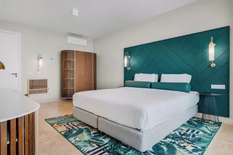 King bed with teal headboard in a guest room at Mangrove Beach Corendon Curacao Resort.