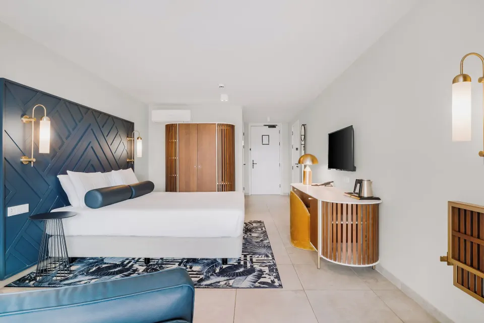 King bed guest room with teal headboard and work desk at Mangrove Beach Corendon Curacao Resort.