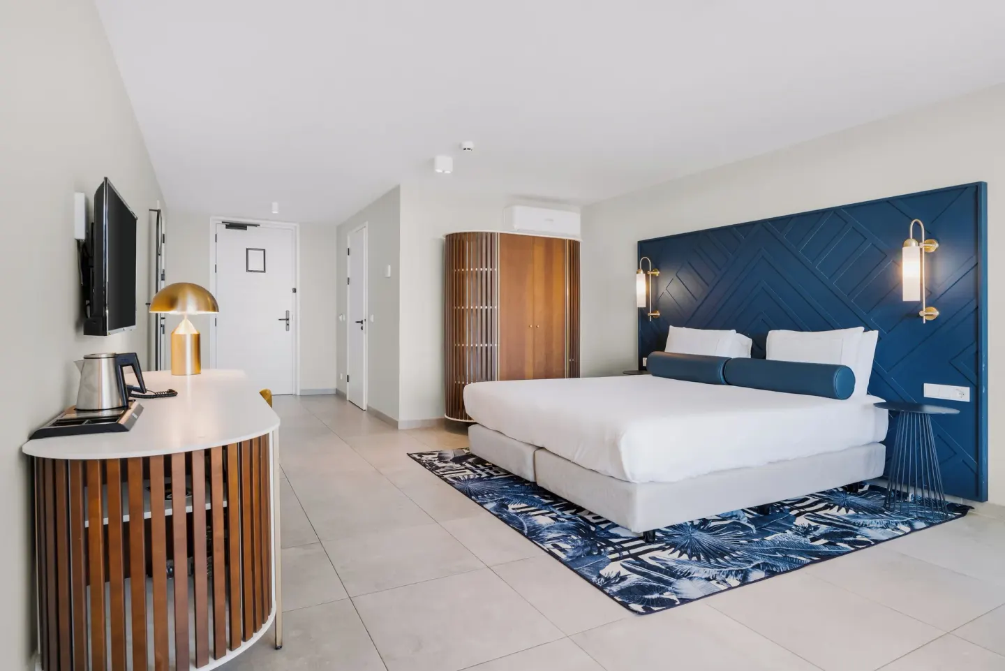 King bed guest room with blue headboard and tropical rug at Mangrove Beach Corendon Curacao Resort.