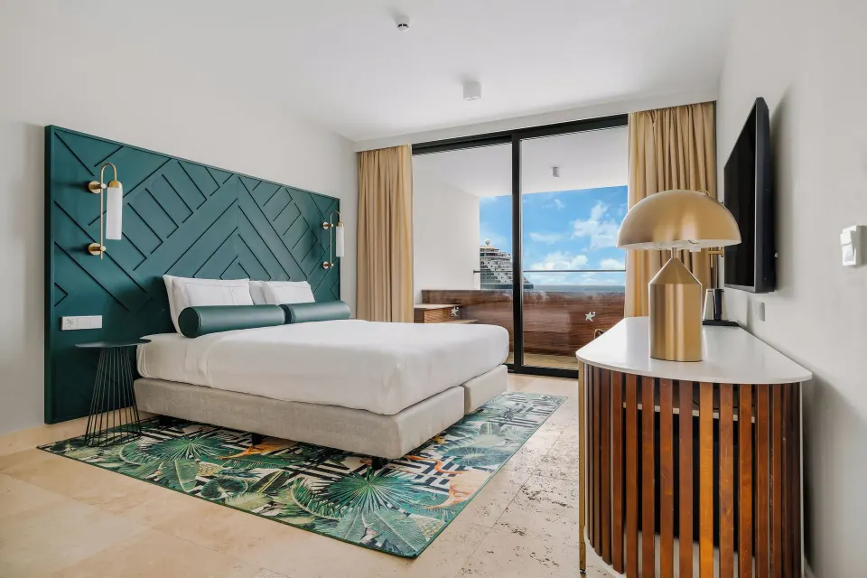 King bed and balcony doors in a guest room at Mangrove Beach Corendon Curacao Resort.