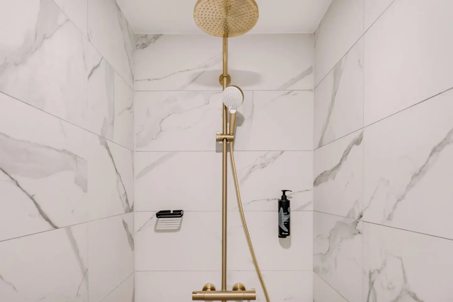 Walk-in shower at Mangrove Beach Corendon Curacao Resort with gold-tone fixtures and marble-look tile.