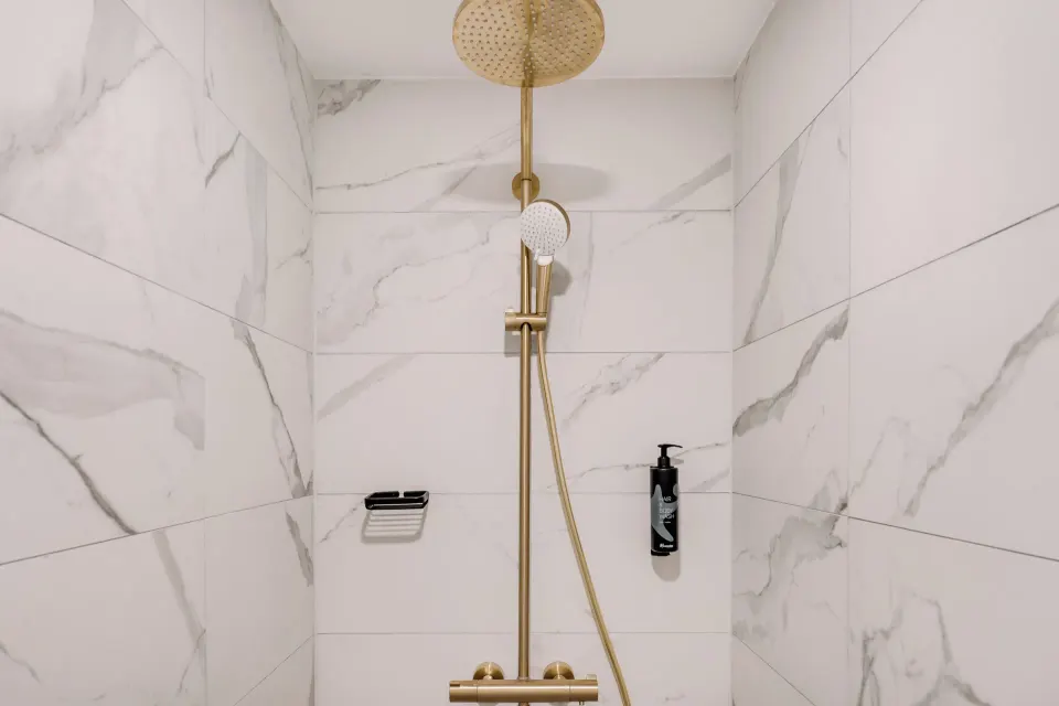 Walk-in shower at Mangrove Beach Corendon Curacao Resort with gold-tone fixtures and marble-look tile.