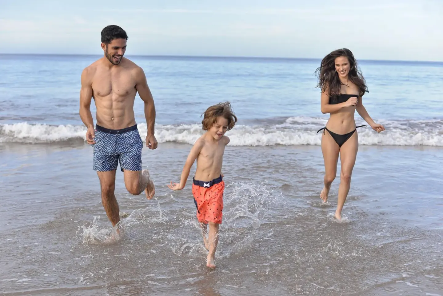 Three guests run through shallow ocean surf near Margaritaville Beach Resort Playa Flamingo.