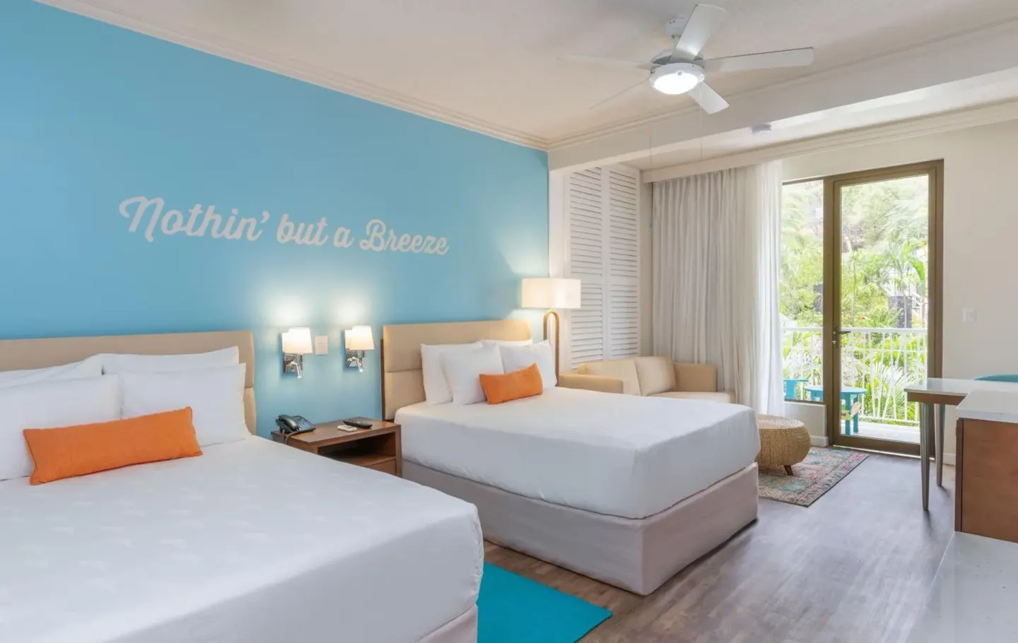 Guest room with two beds, turquoise wall and balcony doors at Margaritaville Beach Resort Playa Flamingo.