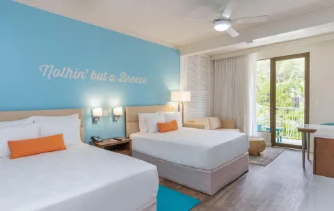 Guest room with two beds, turquoise wall and balcony doors at Margaritaville Beach Resort Playa Flamingo.