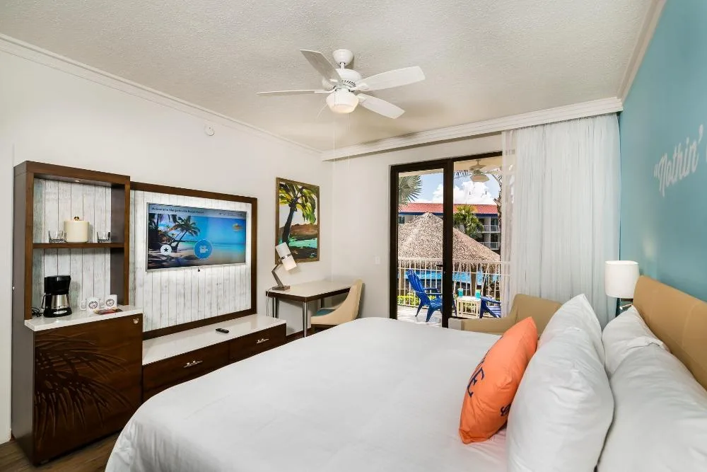 Pool view king bed guest room at Margaritaville Beach Resort Playa Flamingo with balcony doors and TV.