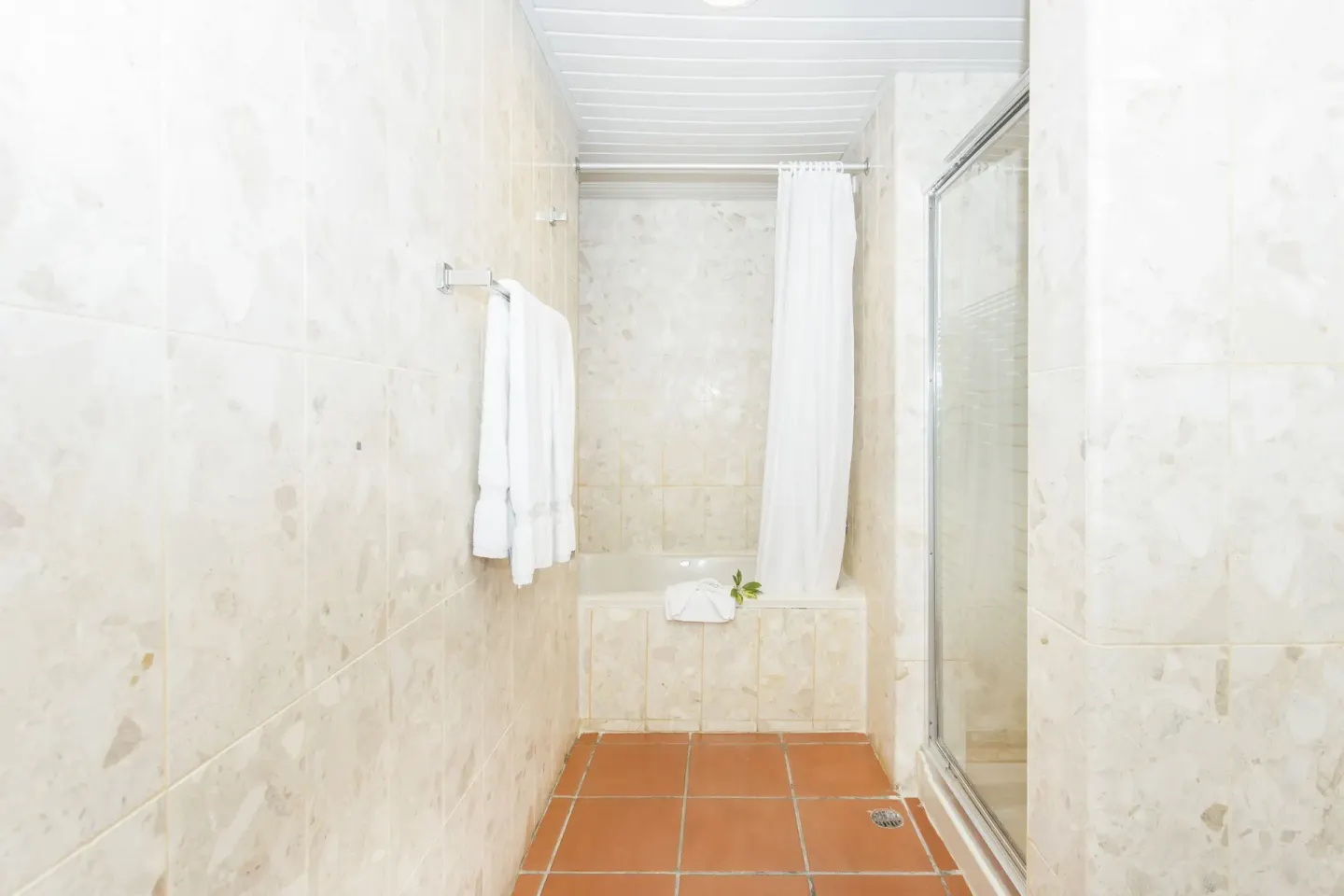 Marble-tiled bathroom with tub, shower curtain and towels at Marien Puerto Plata.