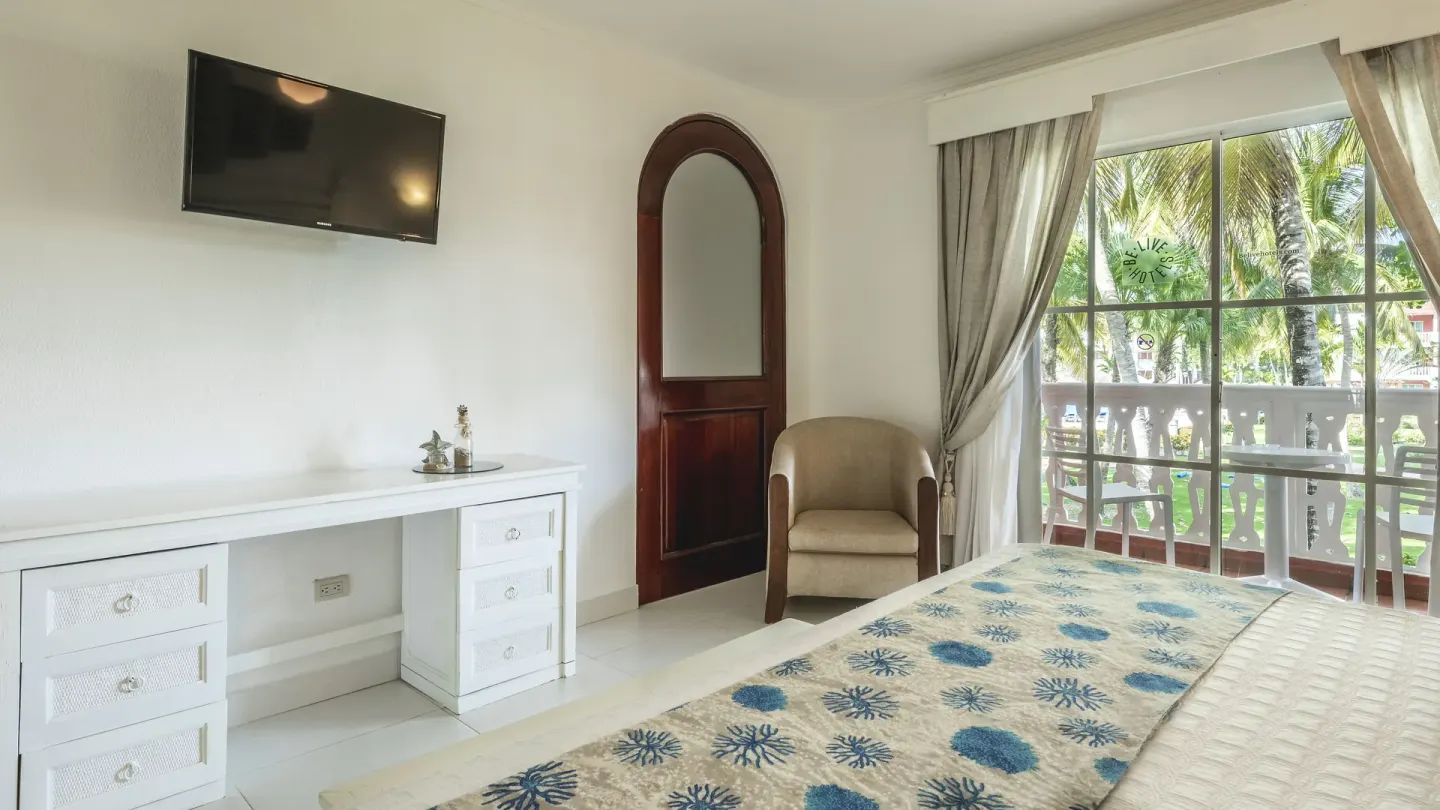 Guest room with bed, desk, TV, armchair, and balcony at Marien Puerto Plata.