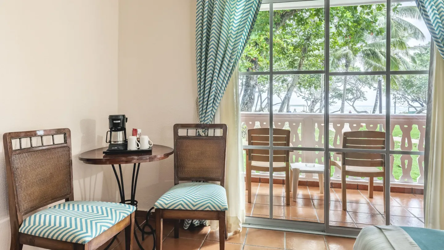 Guest room sitting area with balcony, chairs, coffeemaker, and ocean glimpses at Marien Puerto Plata.