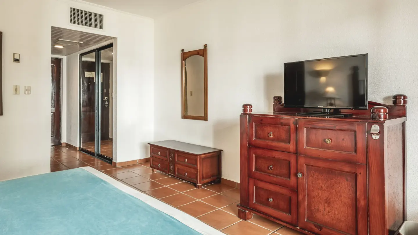Guest room with turquoise bedspread, wood dresser and TV at Marien Puerto Plata.