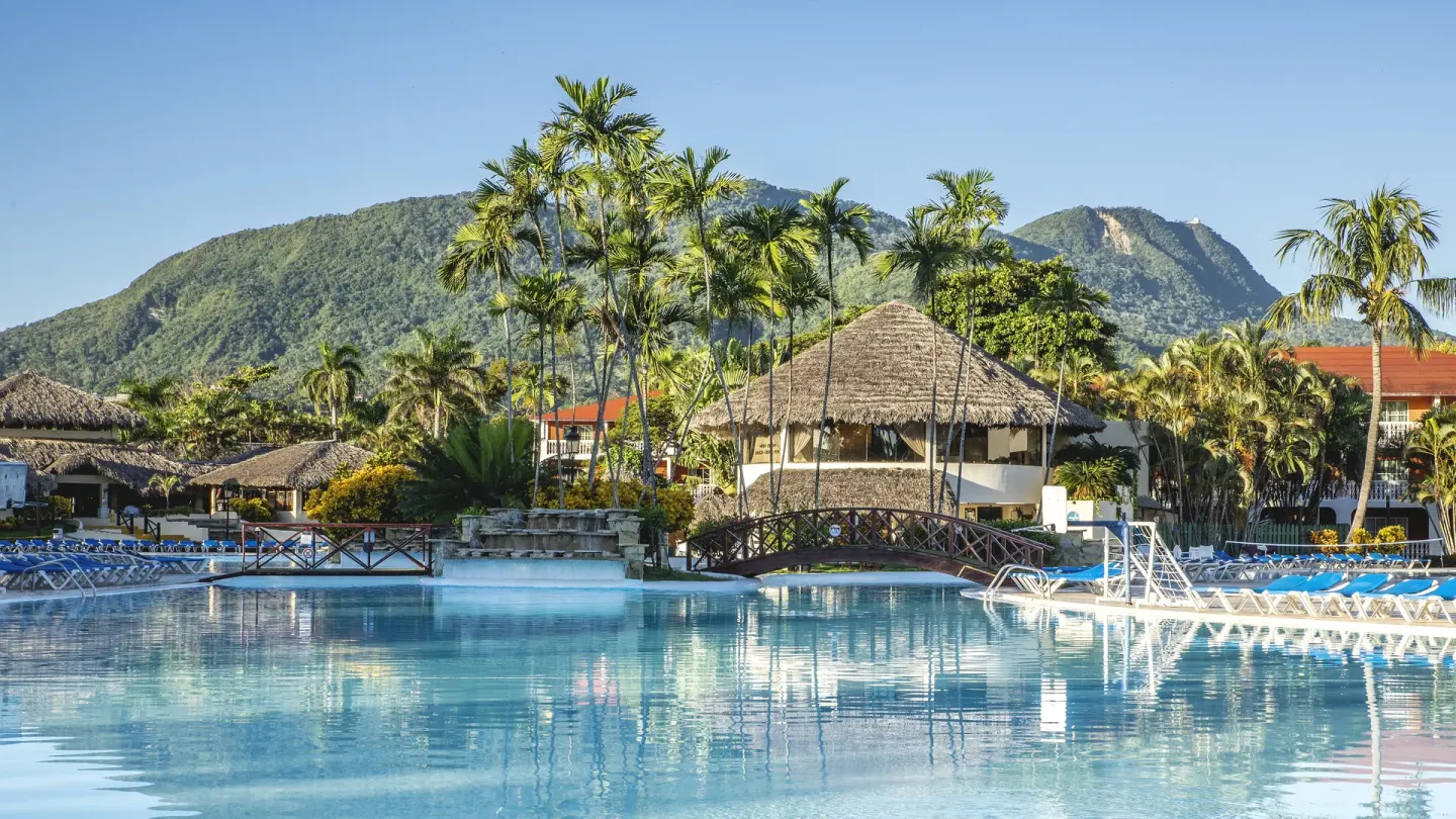 Large resort pool with palms, bridge and mountain backdrop at Marien Puerto Plata.