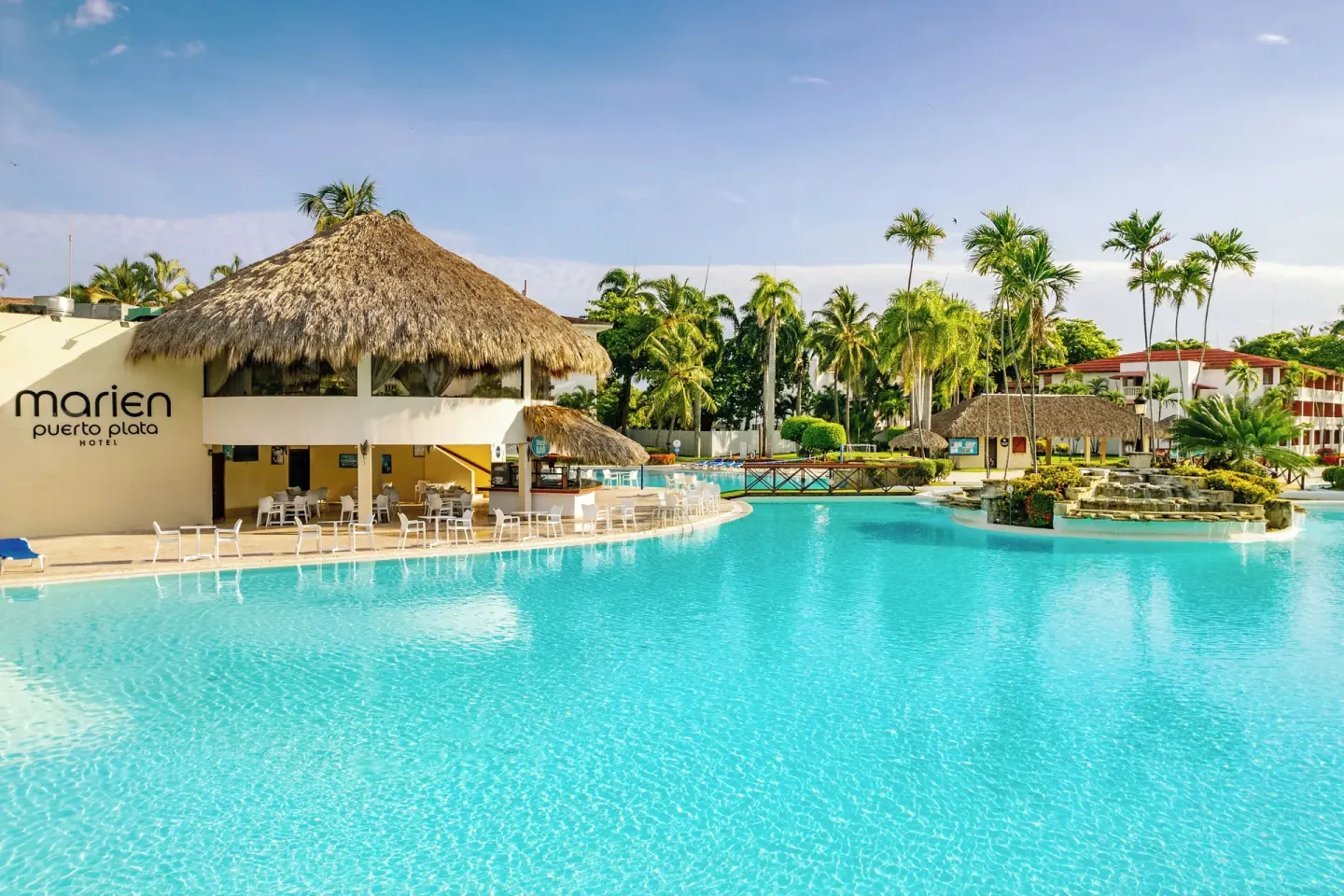 Large resort pool with thatched roofs and palm trees at Marien Puerto Plata.