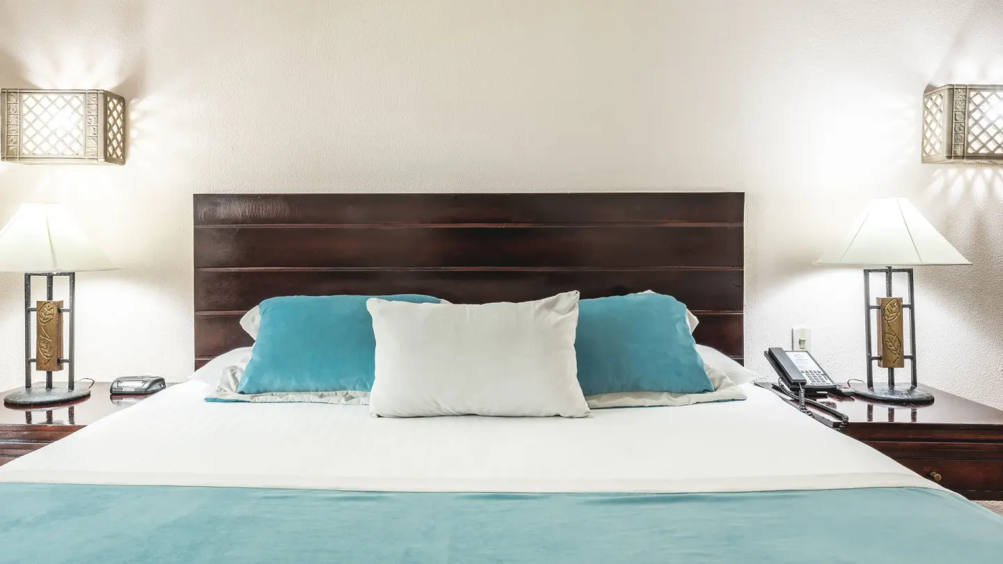King bed with turquoise pillows and bedside lamps in a Deluxe Ocean View room at Marien Puerto Plata.