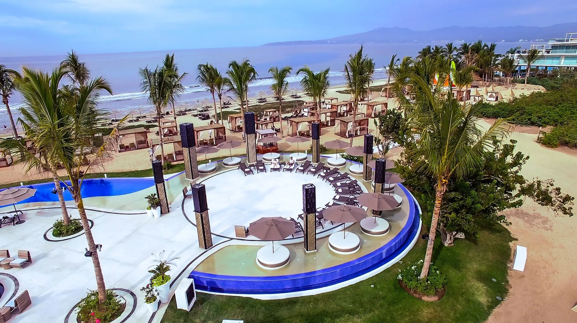 Pool deck, beach cabanas, and palms overlooking the ocean at Marival Distinct World Spa.