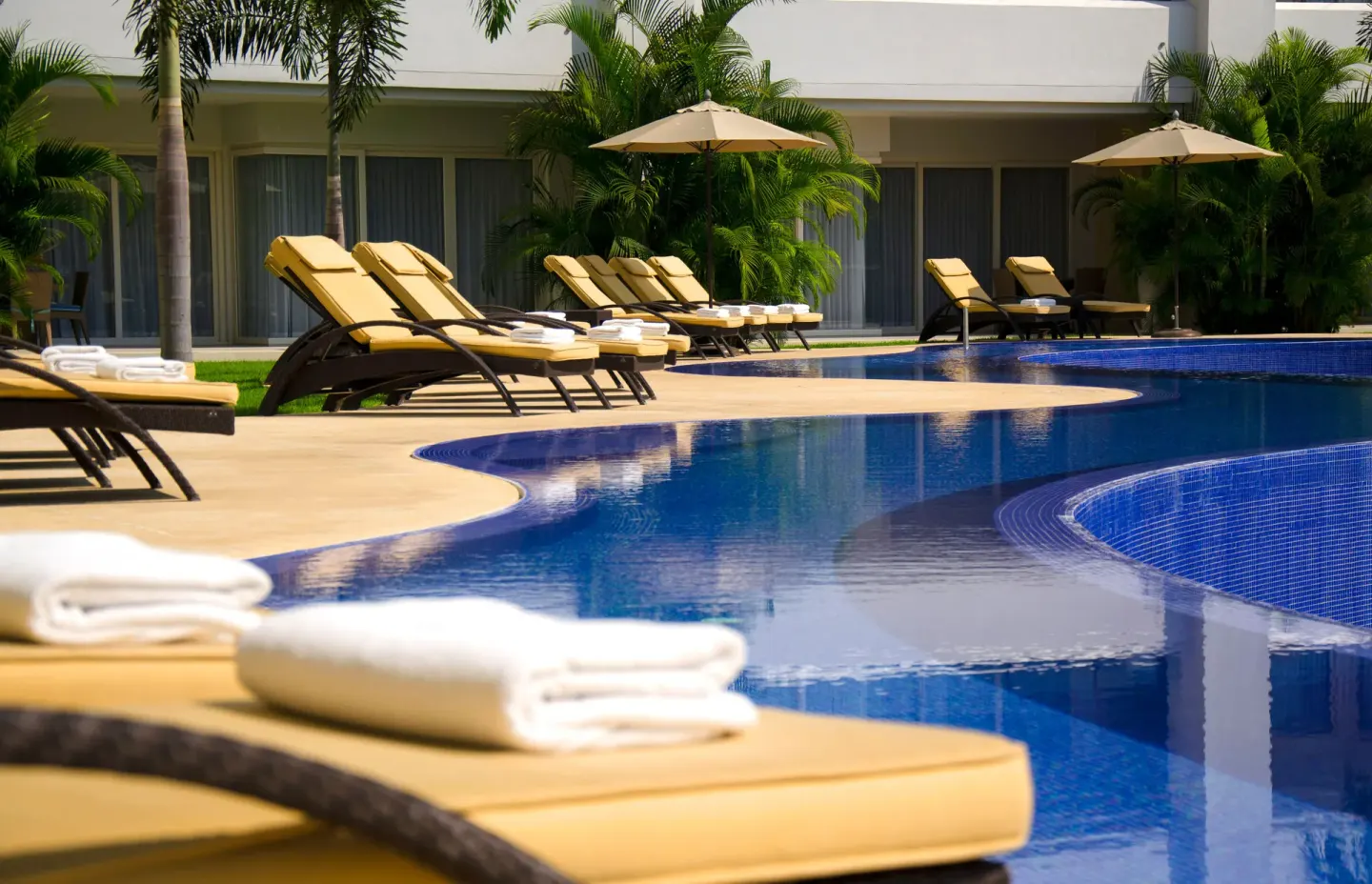 Curved resort pool with cushioned loungers at Marival Distinct World Spa.
