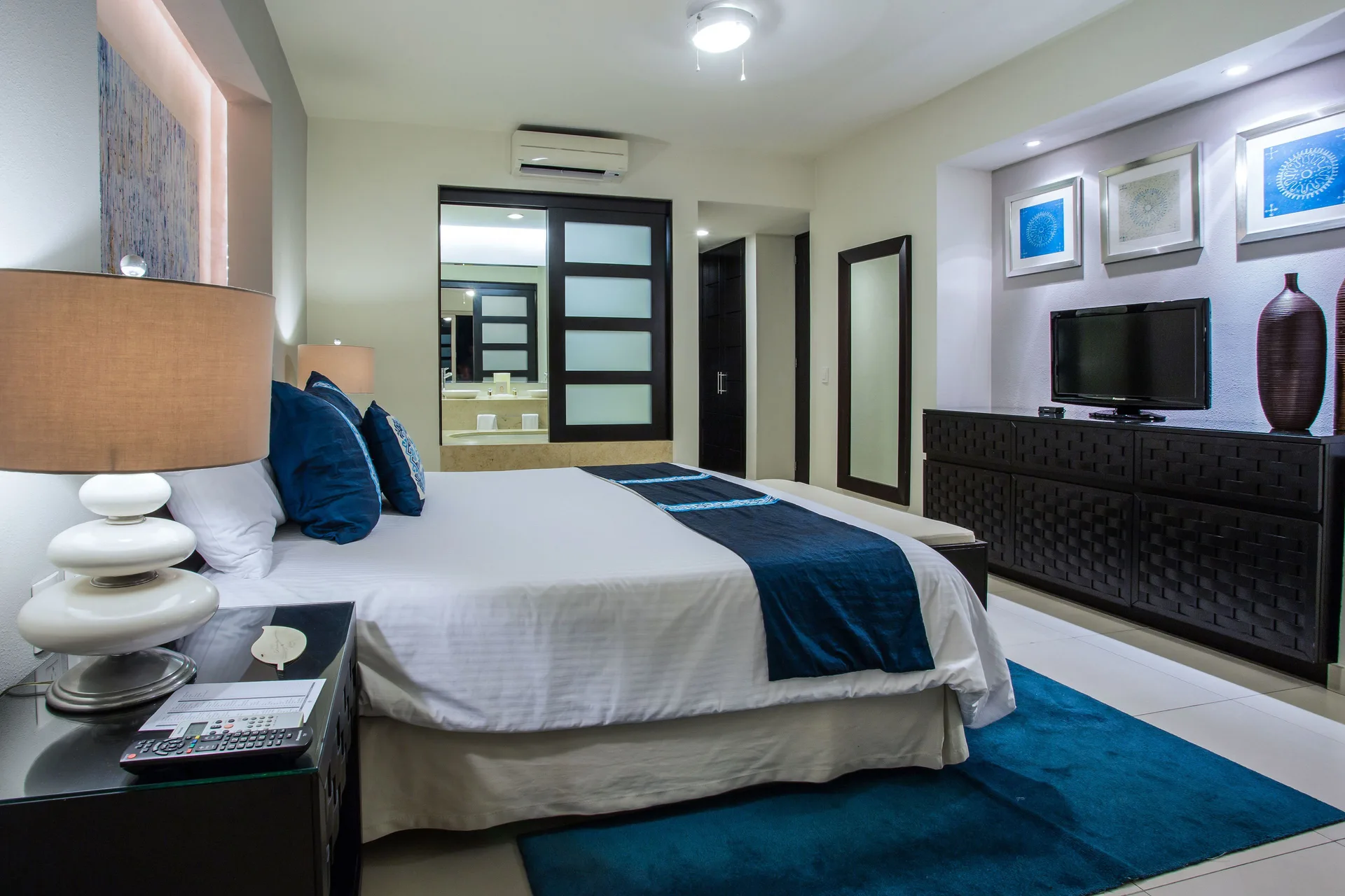 Guest room with king bed, blue accents, TV, and vanity area at Marival Distinct World Spa.