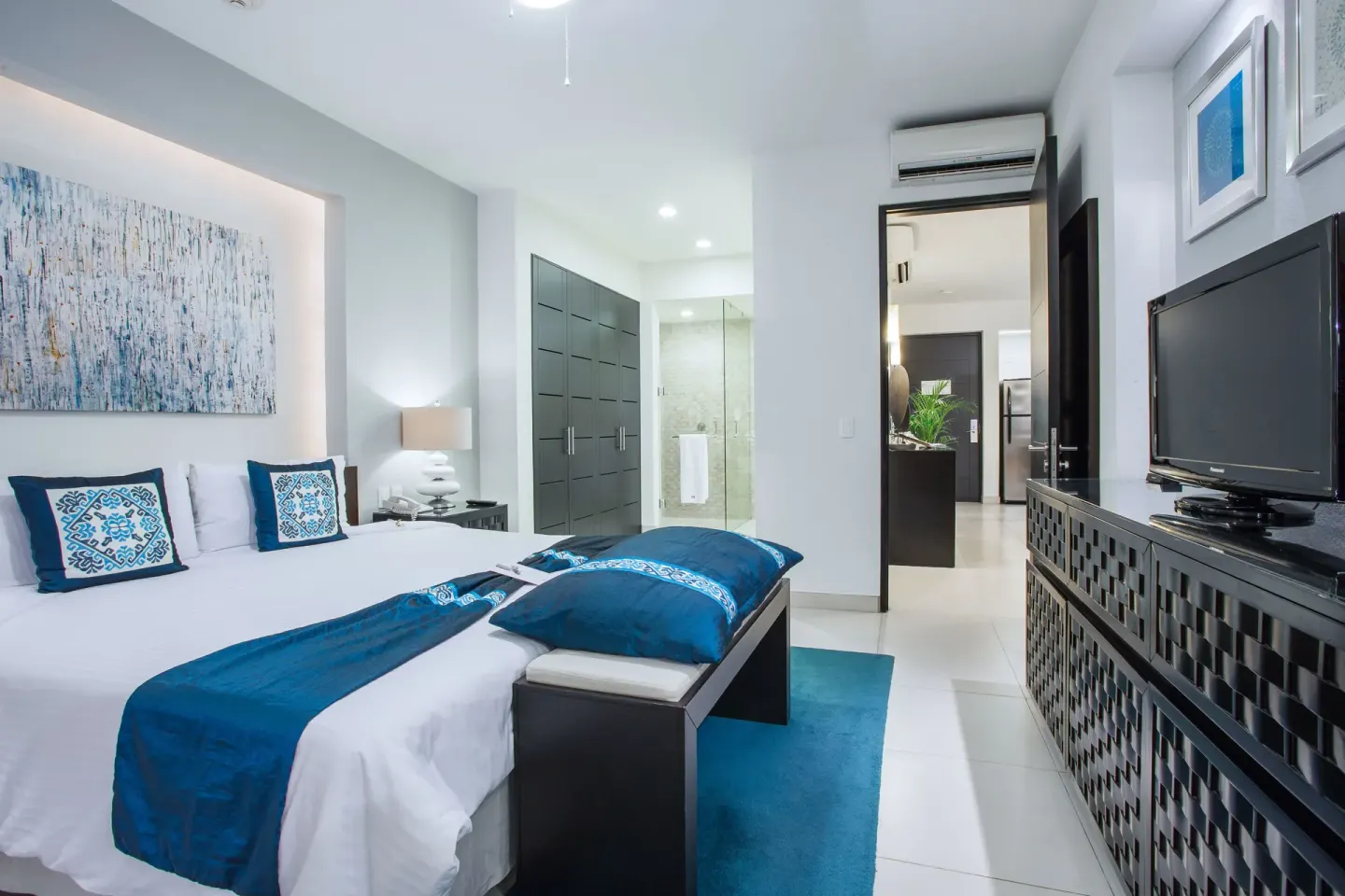 King bedroom with blue accents, TV console, and closet area at Marival Distinct World Spa.