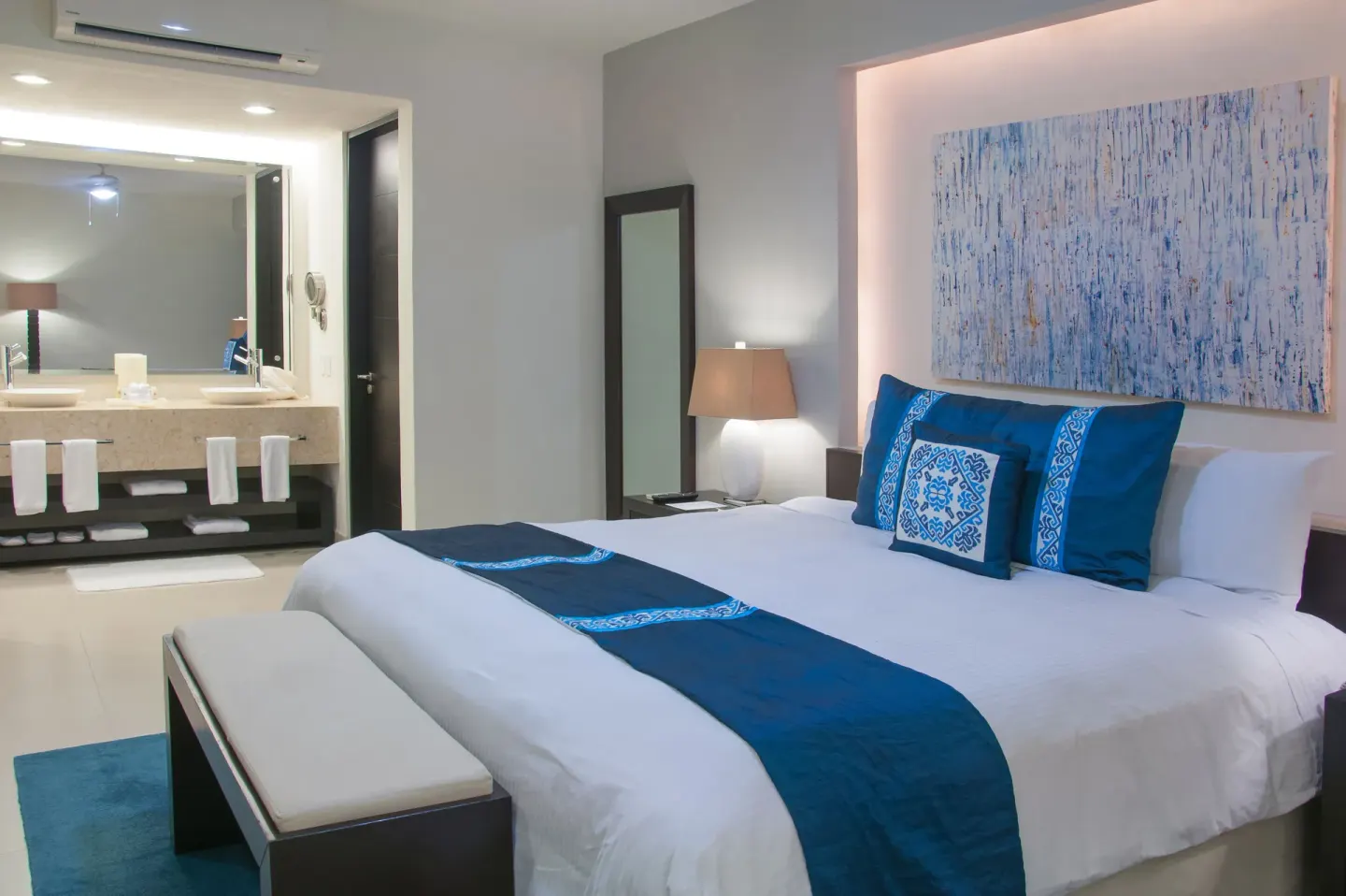 King bed with blue accents and open bathroom vanity at Marival Distinct World Spa.
