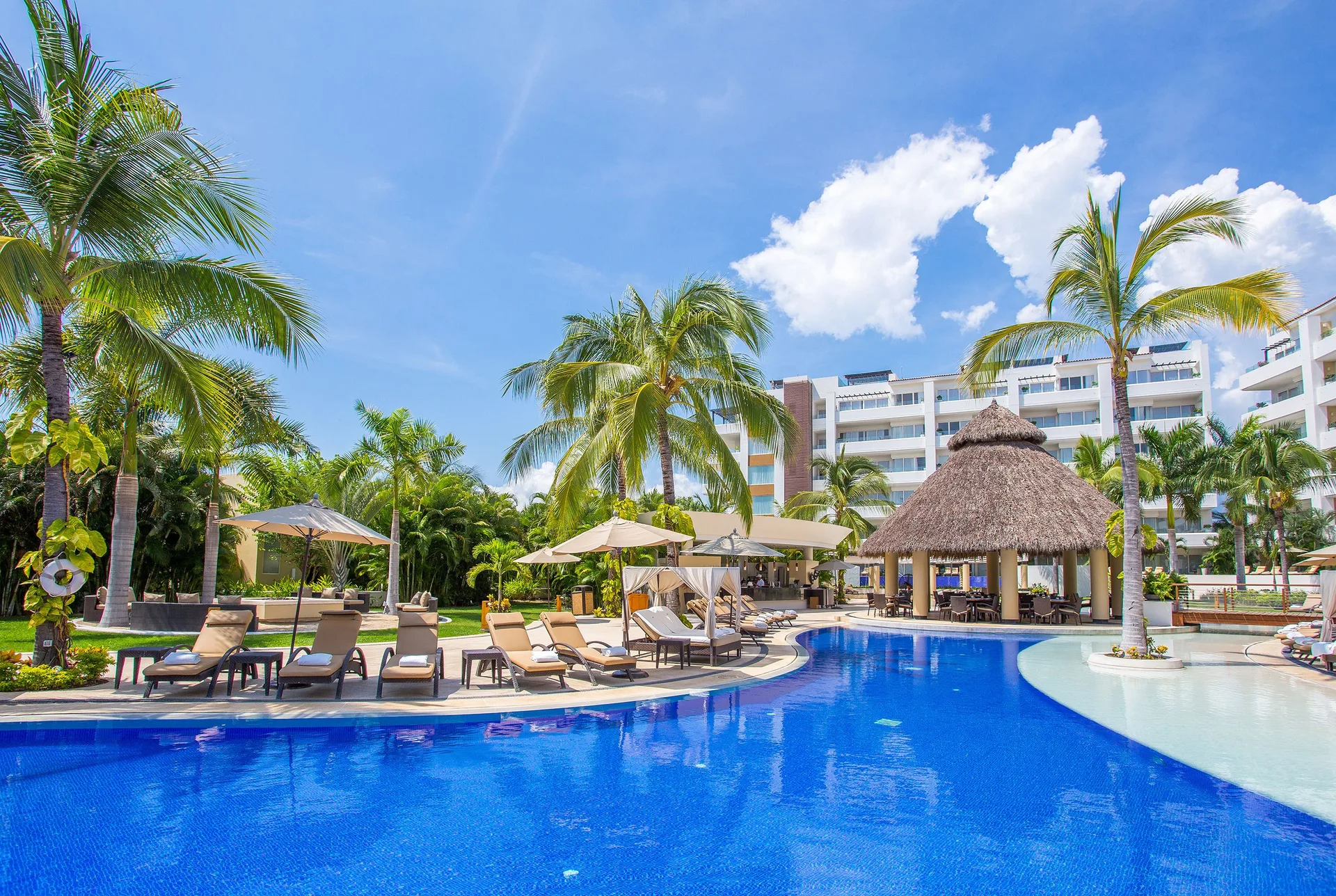 Palm-lined pool with loungers and a palapa at Marival Distinct World Spa.