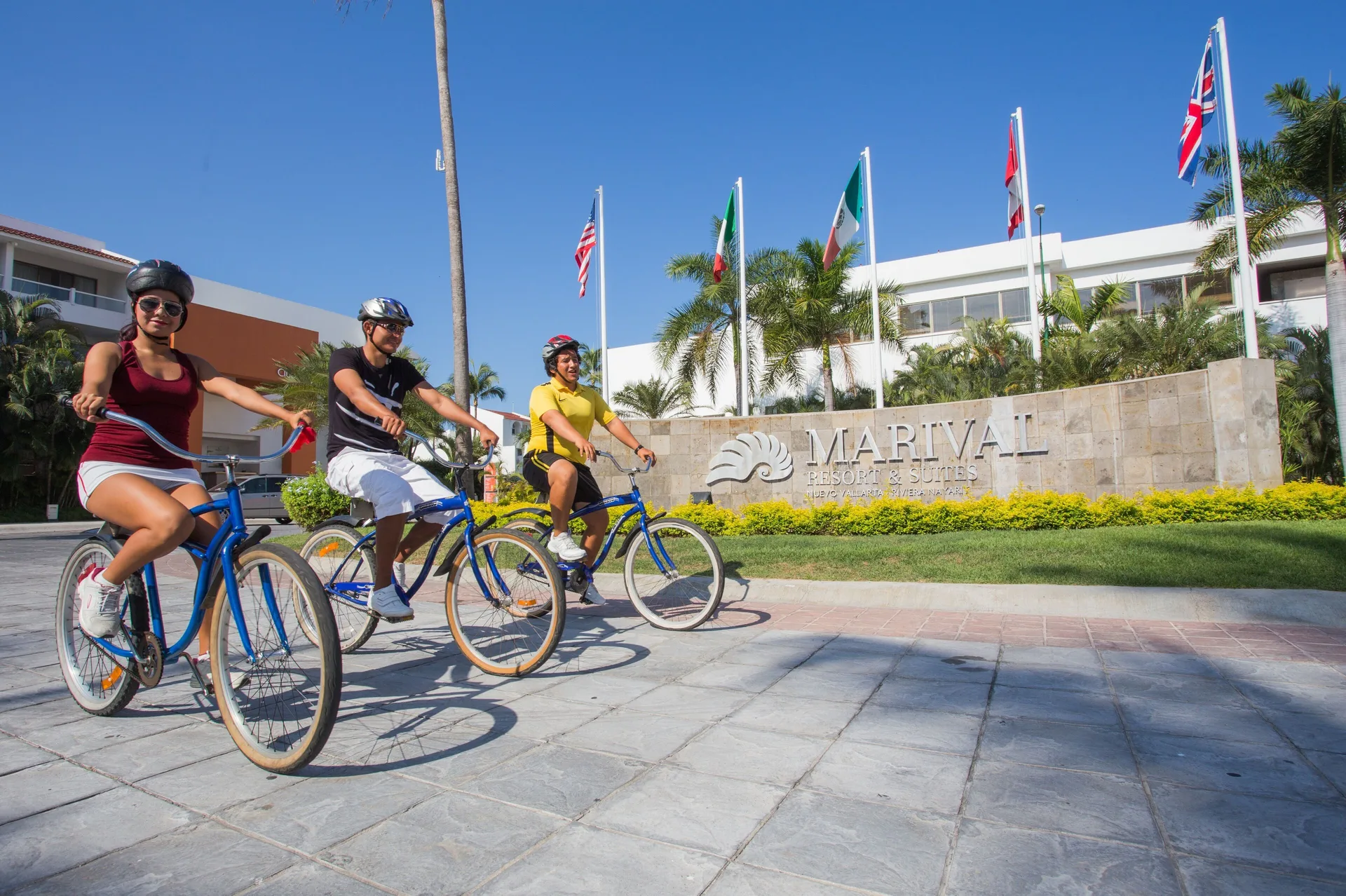 Cyclists ride past the resort entrance sign and flags at Marival Distinct World Spa.