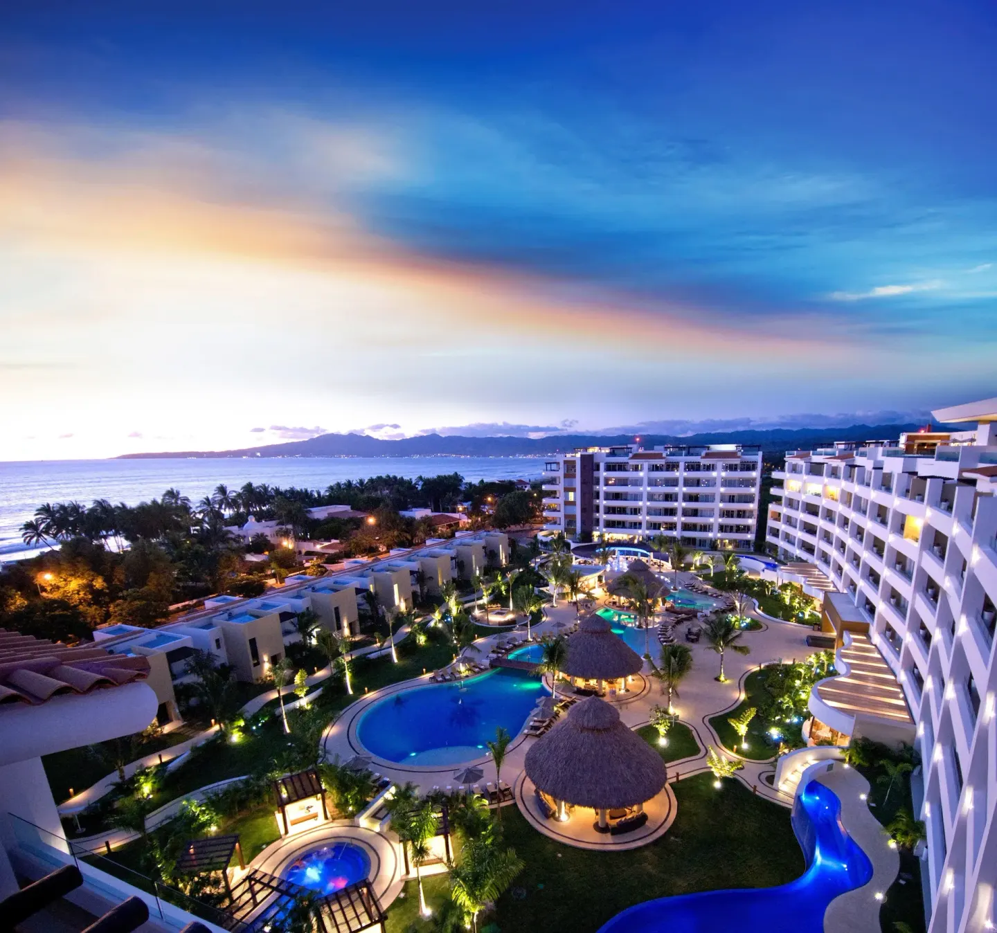 Resort pools, buildings, and ocean at dusk at Marival Distinct World Spa.