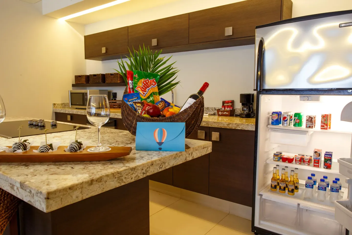 Suite kitchen with granite island, snacks, wine, and open refrigerator at Marival Distinct World Spa.