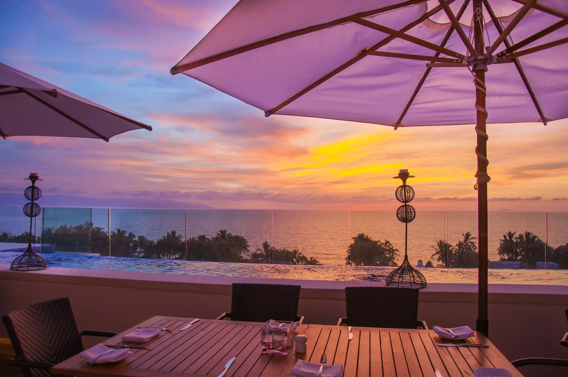 Rooftop dining table by an infinity pool at sunset at Marival Distinct World Spa.