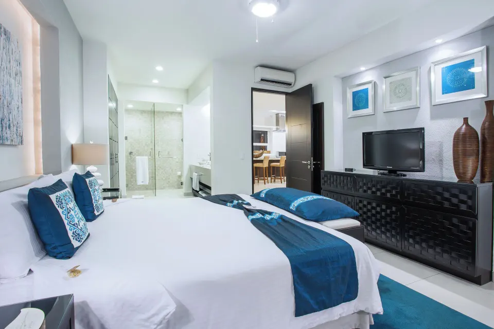 One-Bedroom Suite bedroom with bed, TV, and glass shower at Marival Distinct World Spa.