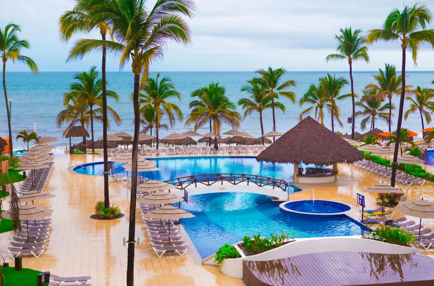 Elevated view of the beachside pool, loungers, palms, and ocean at Marival Emotions Resort.
