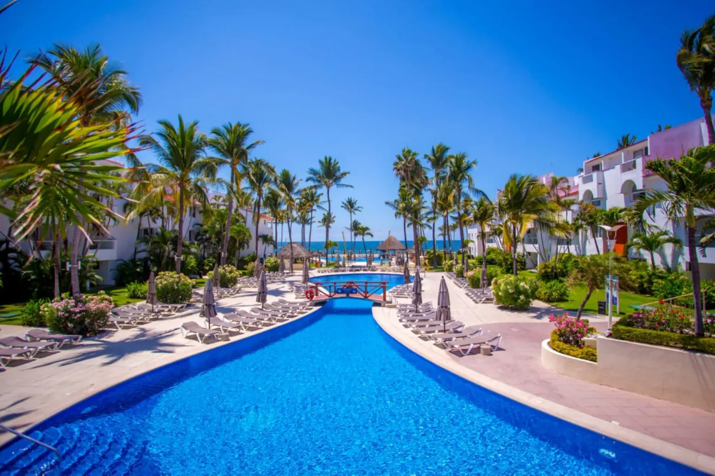 Curving resort pool with palm trees, loungers, and garden paths at Marival Emotions Resort.