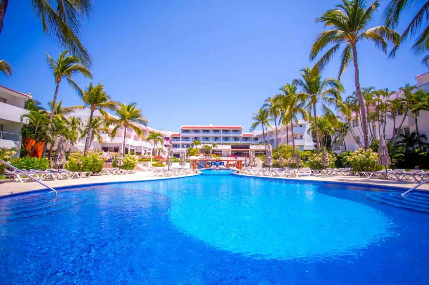 Main pool with palms and resort buildings at Marival Emotions Resort.