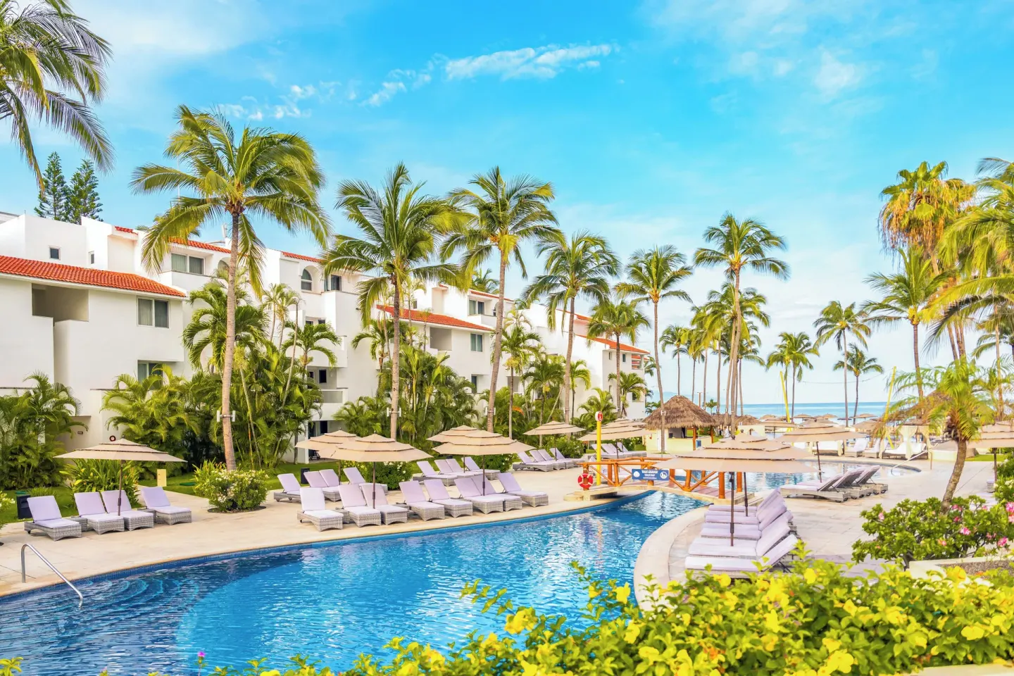 Curved pool lined with loungers and palm trees at Marival Emotions Resort.
