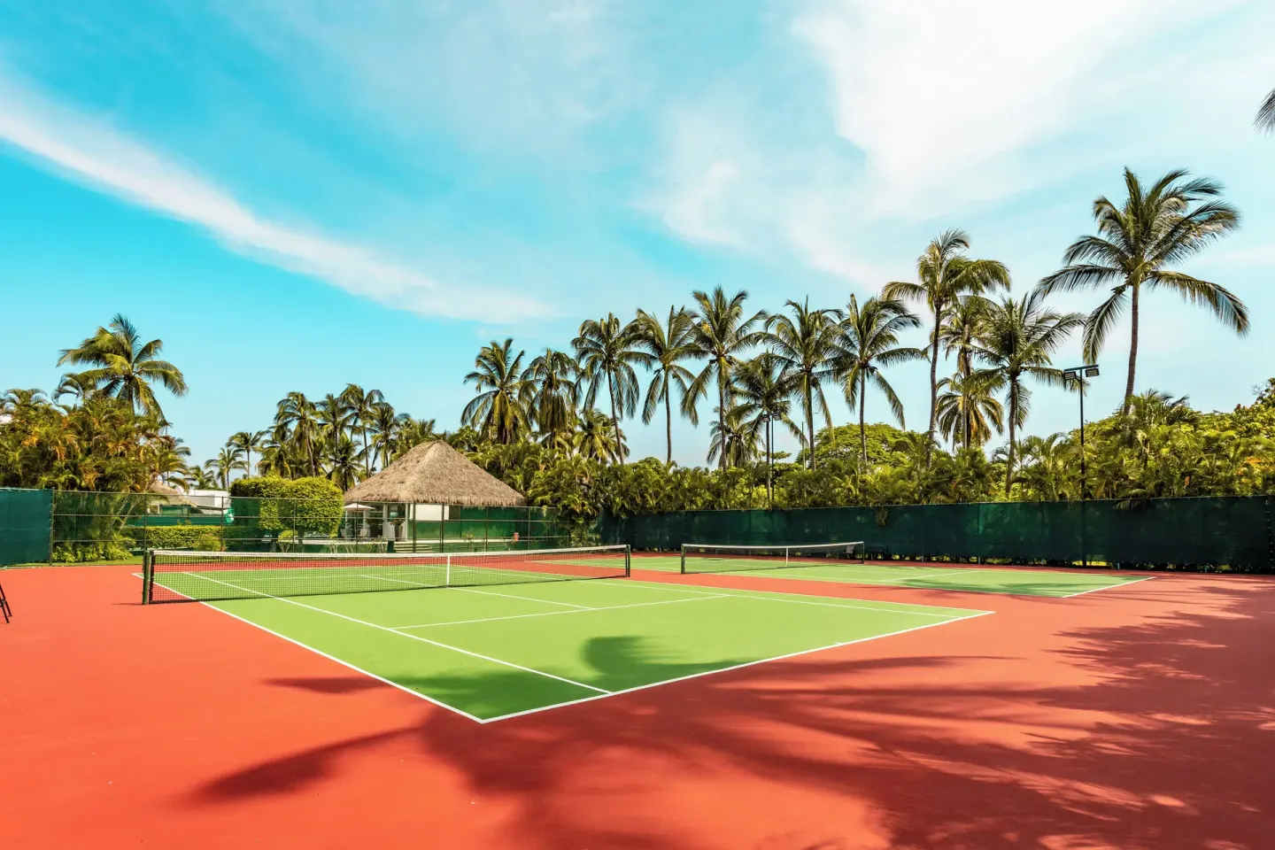 Empty tennis court framed by palm trees at Marival Emotions Resort.