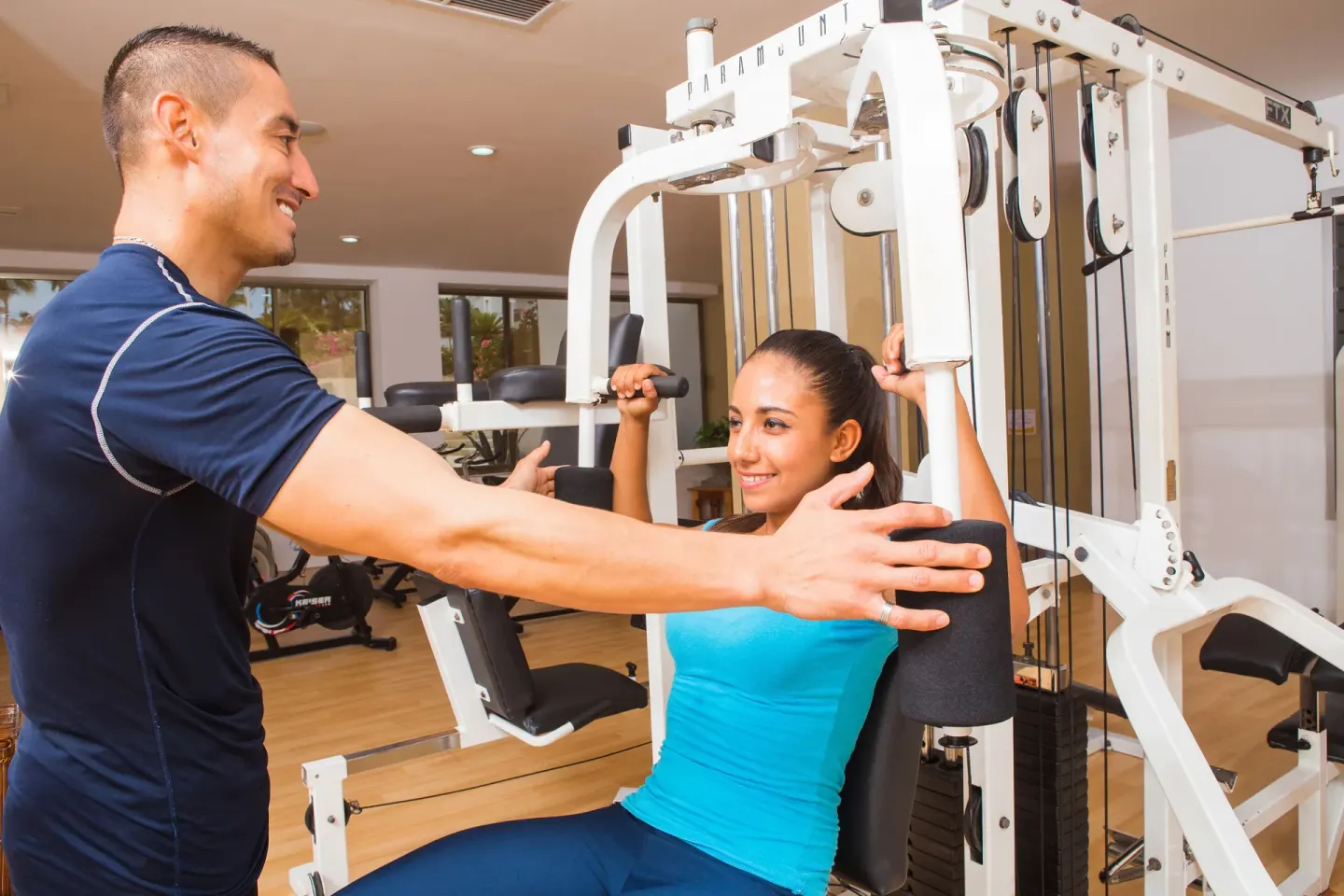 Trainer guides a guest on a weight machine in the gym at Marival Emotions Resort.