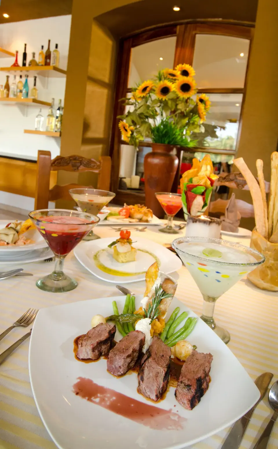Plated entrées, cocktails, breadsticks, and sunflowers on a table at Marival Emotions Resort.