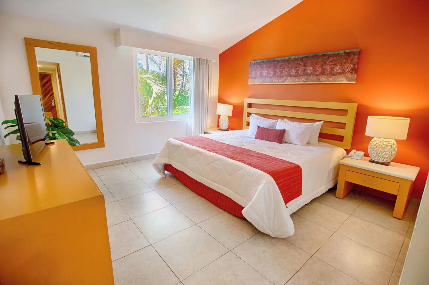 Grand Room with one bed, orange accent wall, dresser, and window at Marival Emotions Resort.