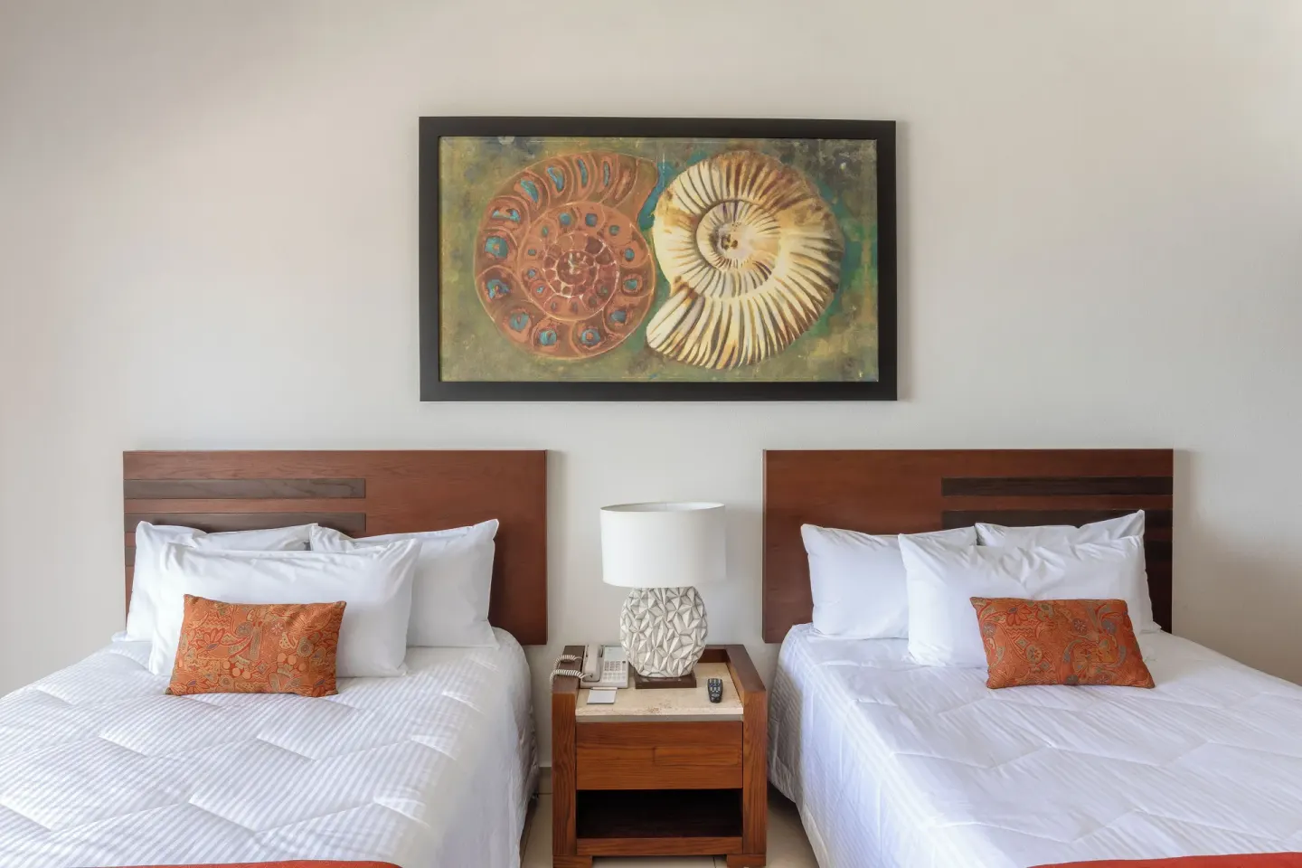 Two beds with a shared nightstand and shell artwork in a Grand Room at Marival Emotions Resort.