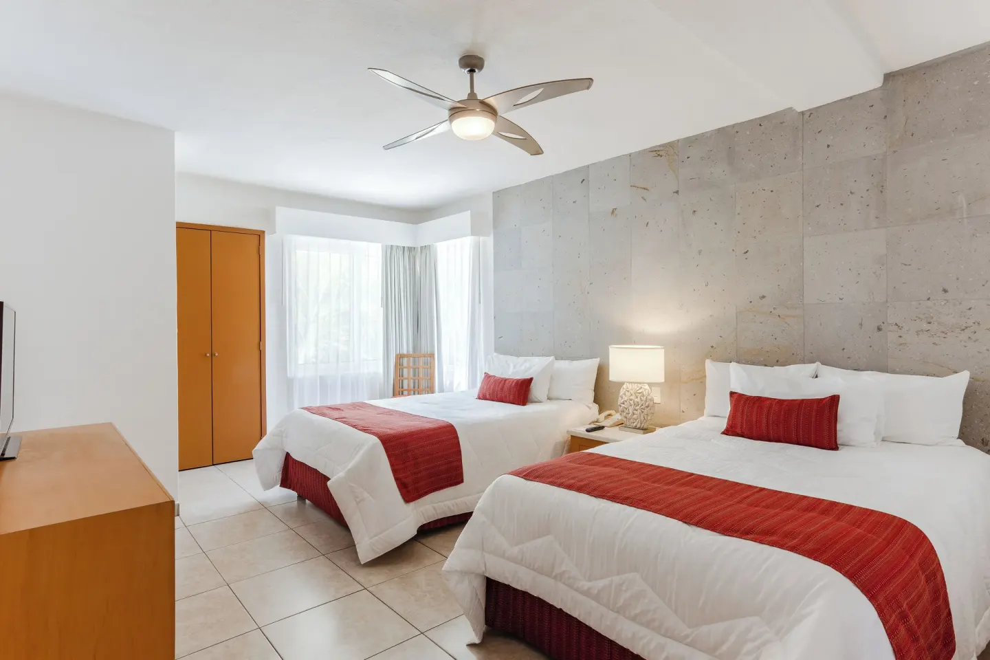 Grand Room with two beds, stone accent wall, dresser, and window at Marival Emotions Resort.
