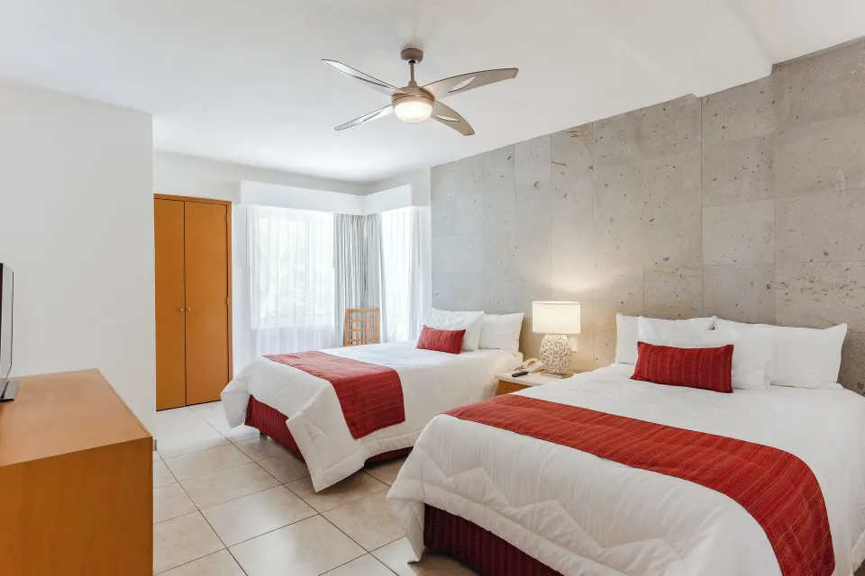 Grand Room with two beds, stone accent wall, dresser, and window at Marival Emotions Resort.