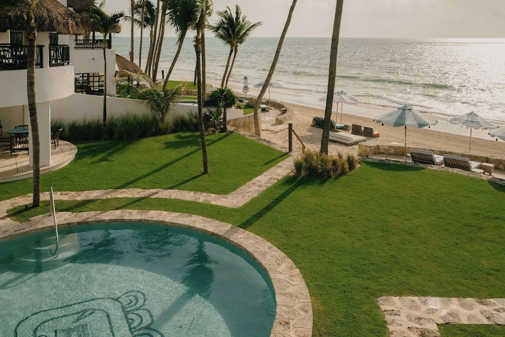 Beachfront lawn, round pool, palms and oceanfront loungers at Maroma, Riviera Maya.